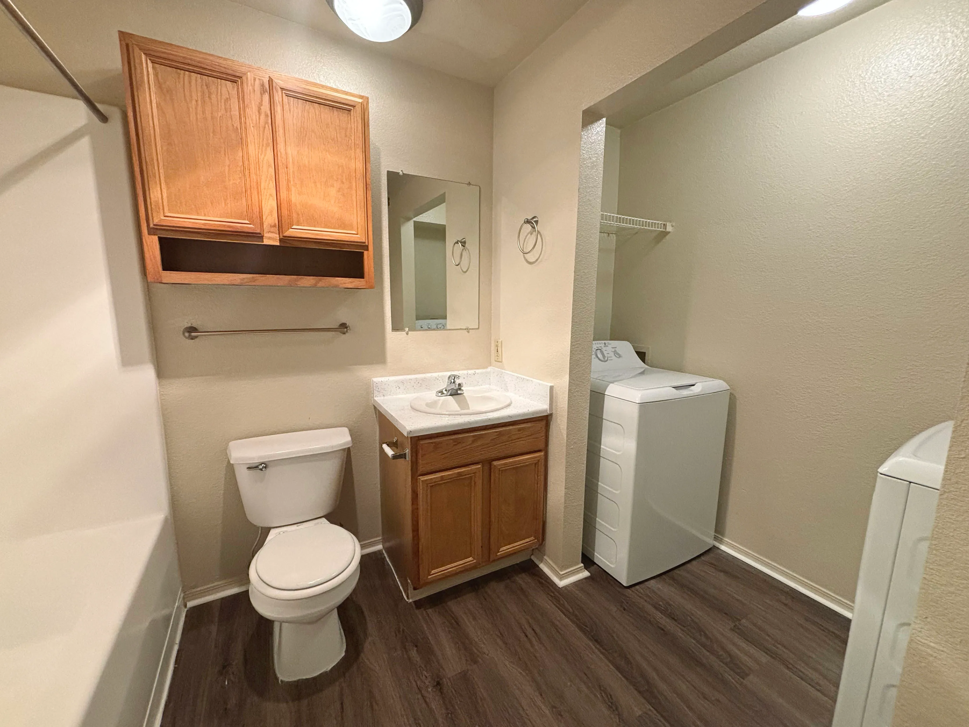 Cozy bathroom featuring wooden cabinetry, a modern washer and dryer, and elegant wood flooring.