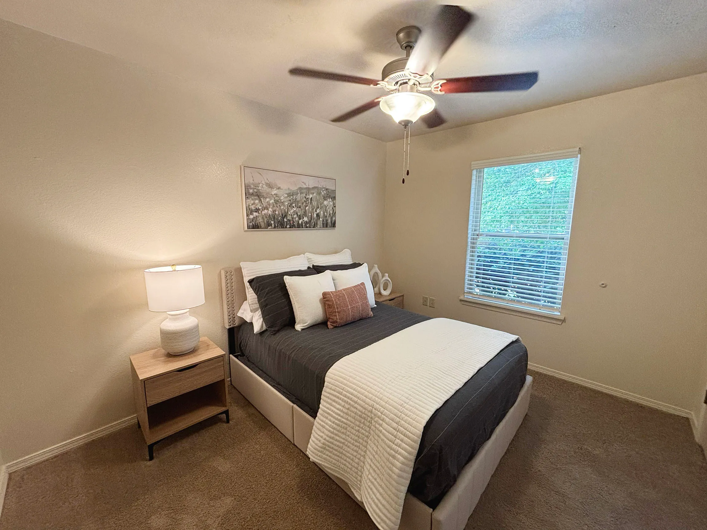 Cozy bedroom with elegant decor, featuring a comfortable bed with plush pillows, a modern ceiling fan, and a window allowing natural light.