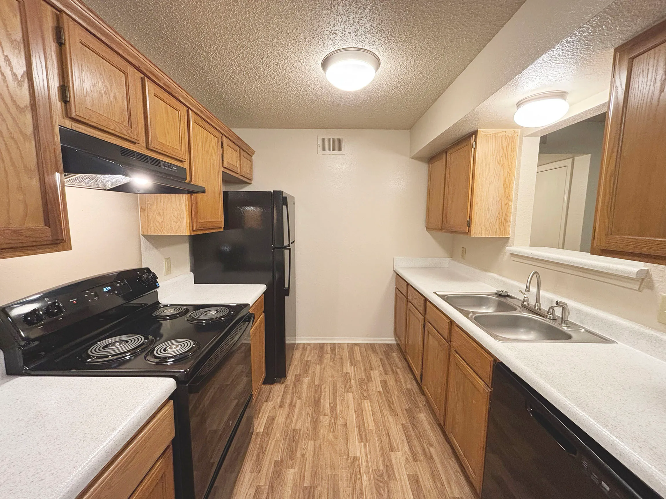Inviting kitchen with warm wood cabinetry, sleek black appliances, and elegant wood-style flooring.