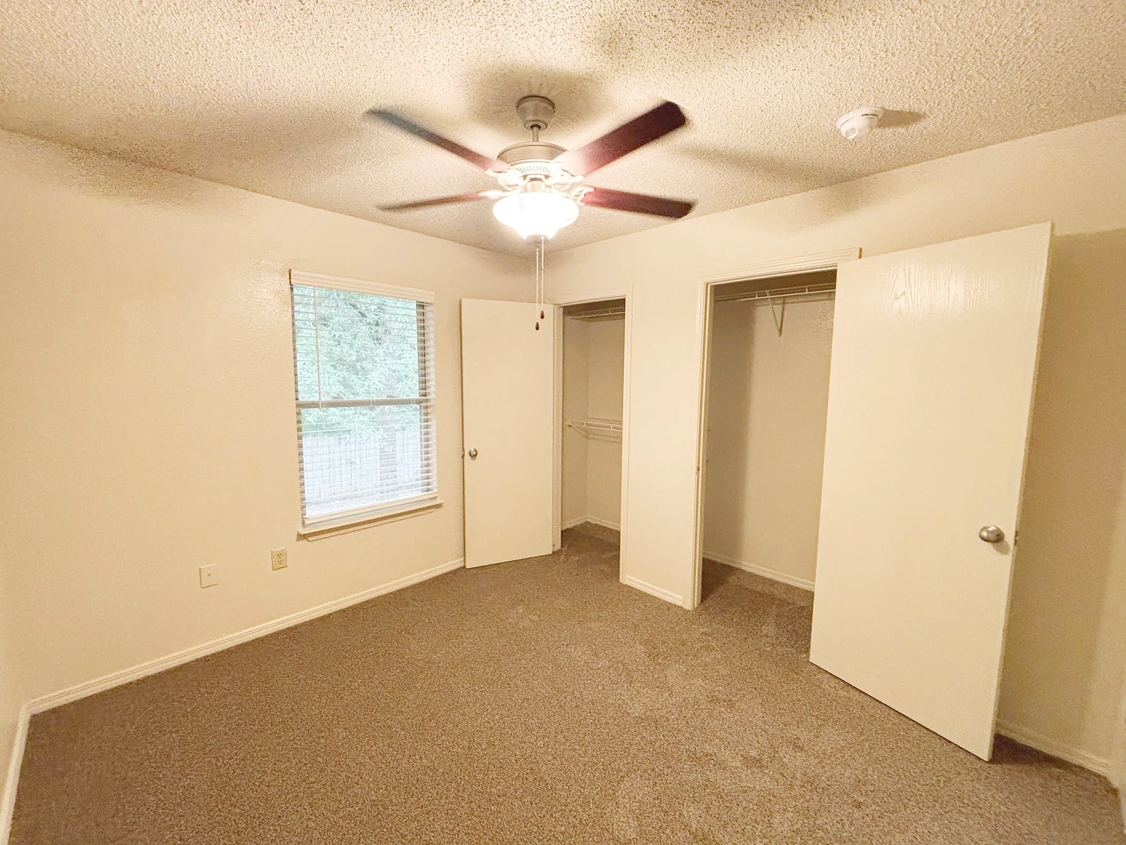 Bright and spacious bedroom featuring a ceiling fan, large window with natural light, and ample closet space with open doors.