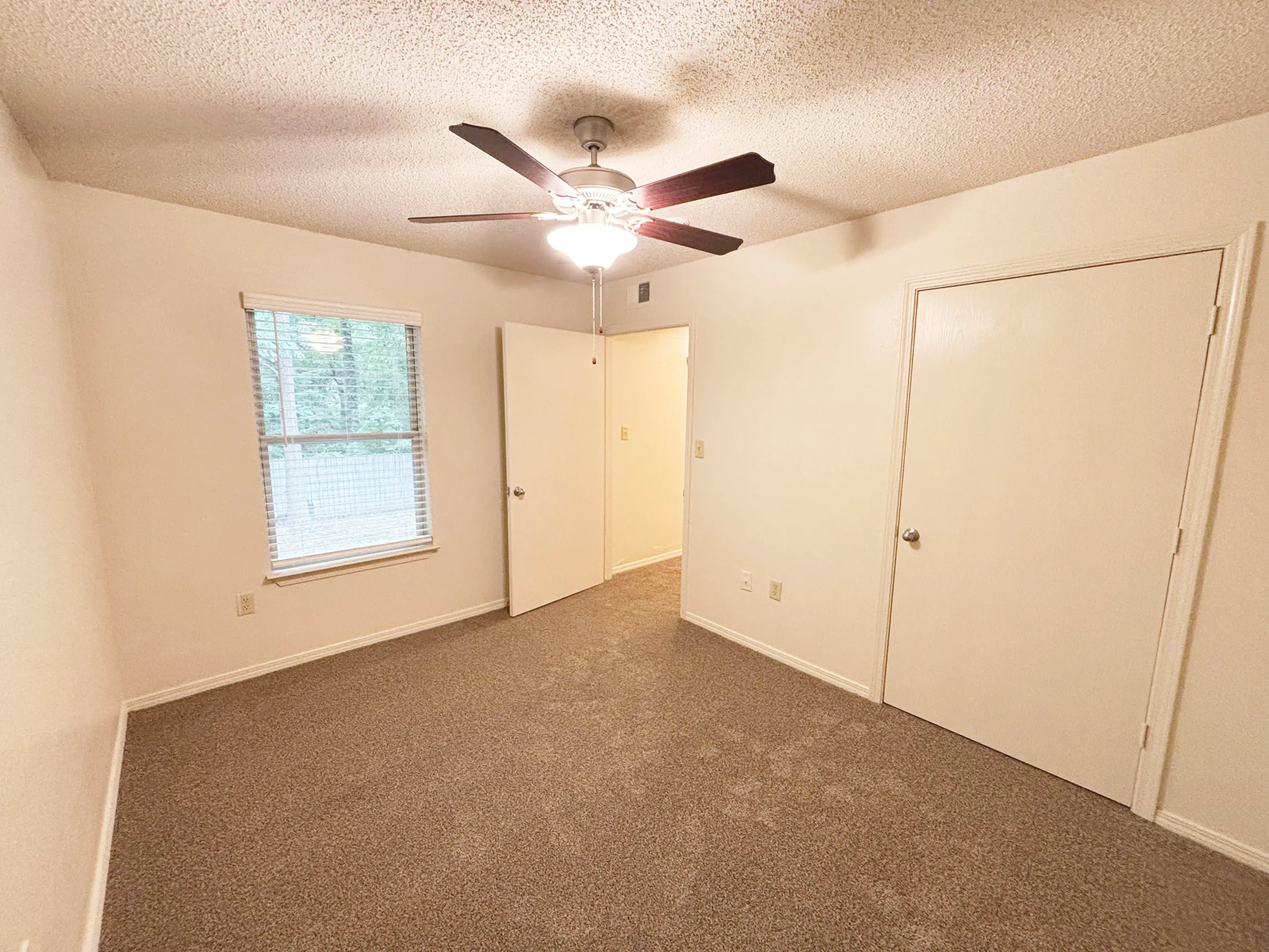 Bright bedroom with soft carpeting, ceiling fan, and ample natural light from window.