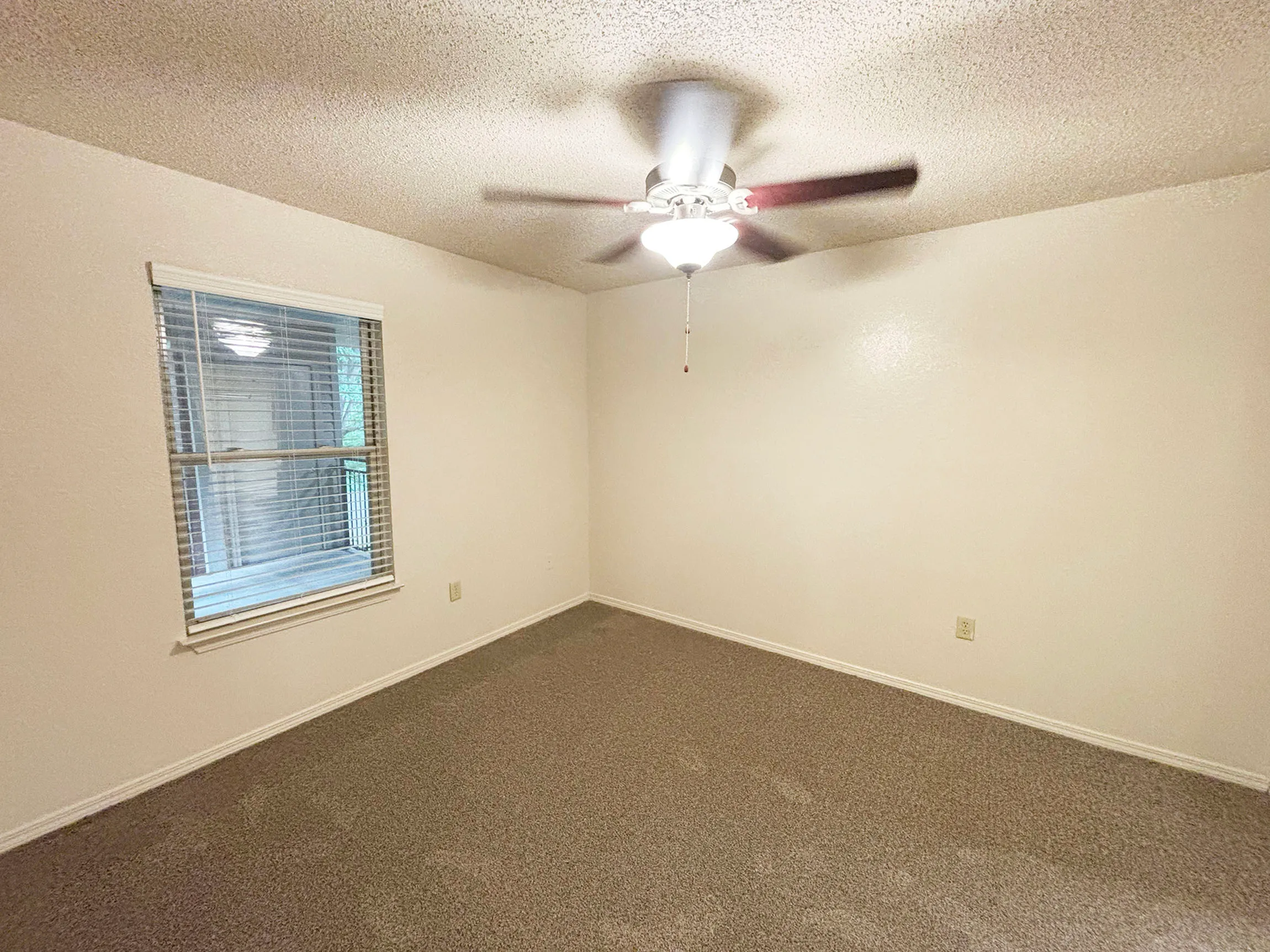 Bright and airy bedroom with a ceiling fan, soft carpeting, and a window offering natural light.
