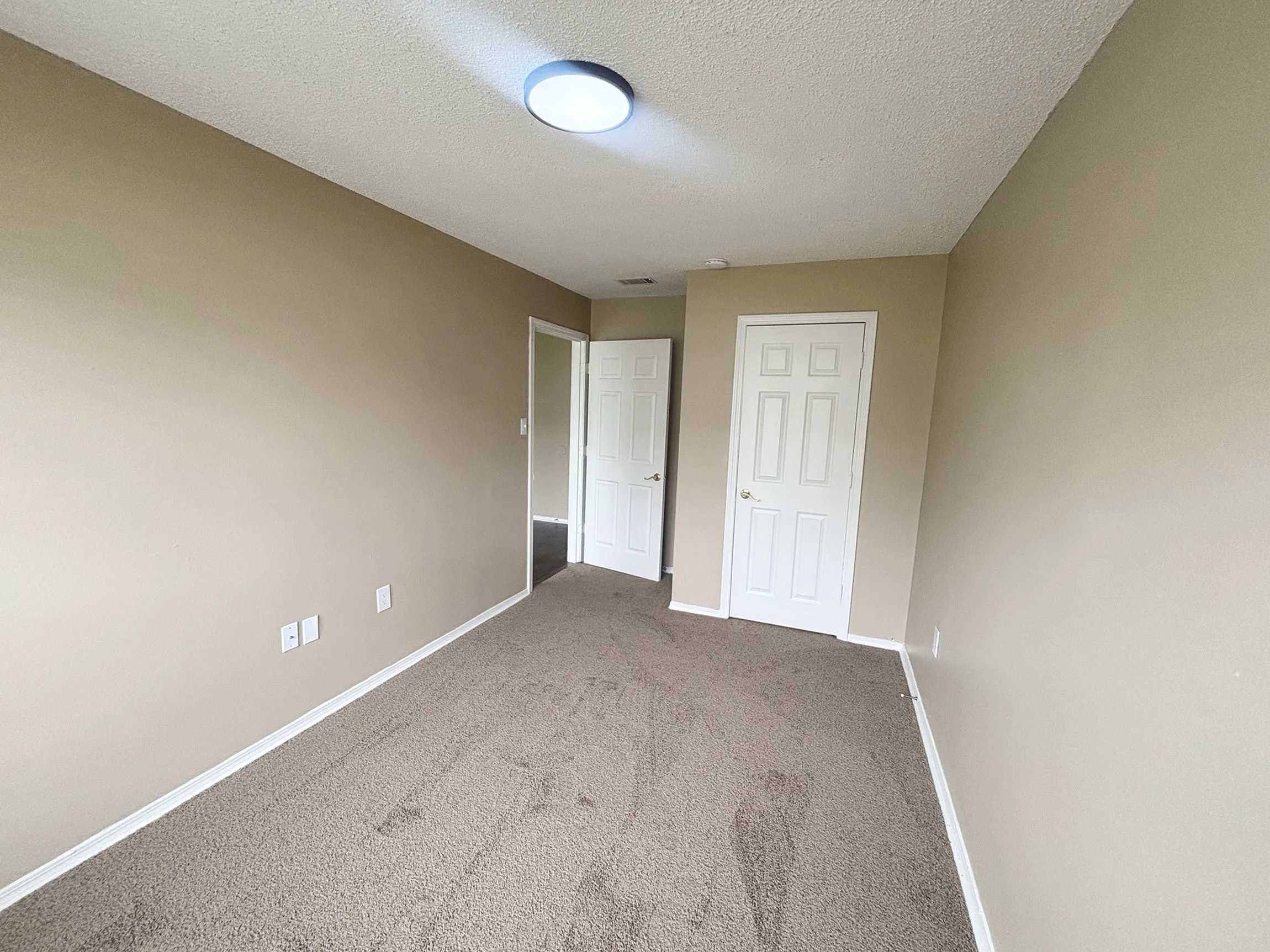 Bright and cozy room with soft carpet and neutral walls, featuring modern lighting and double-door closet.