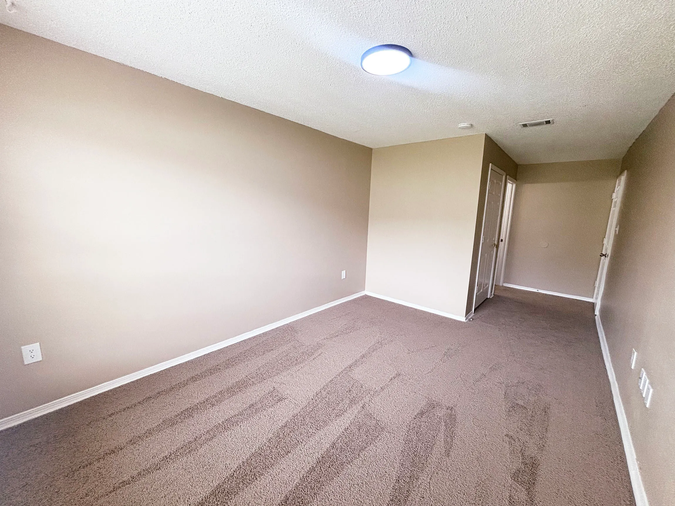 Inviting interior of a spacious room with soft beige walls and cozy carpet flooring, illuminated by modern ceiling light.