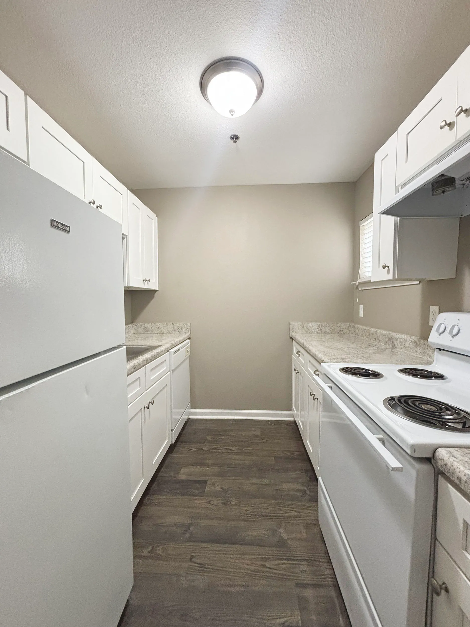 Modern kitchen with sleek white cabinetry, elegant countertops, and stainless steel appliances, set on stylish dark wood flooring.