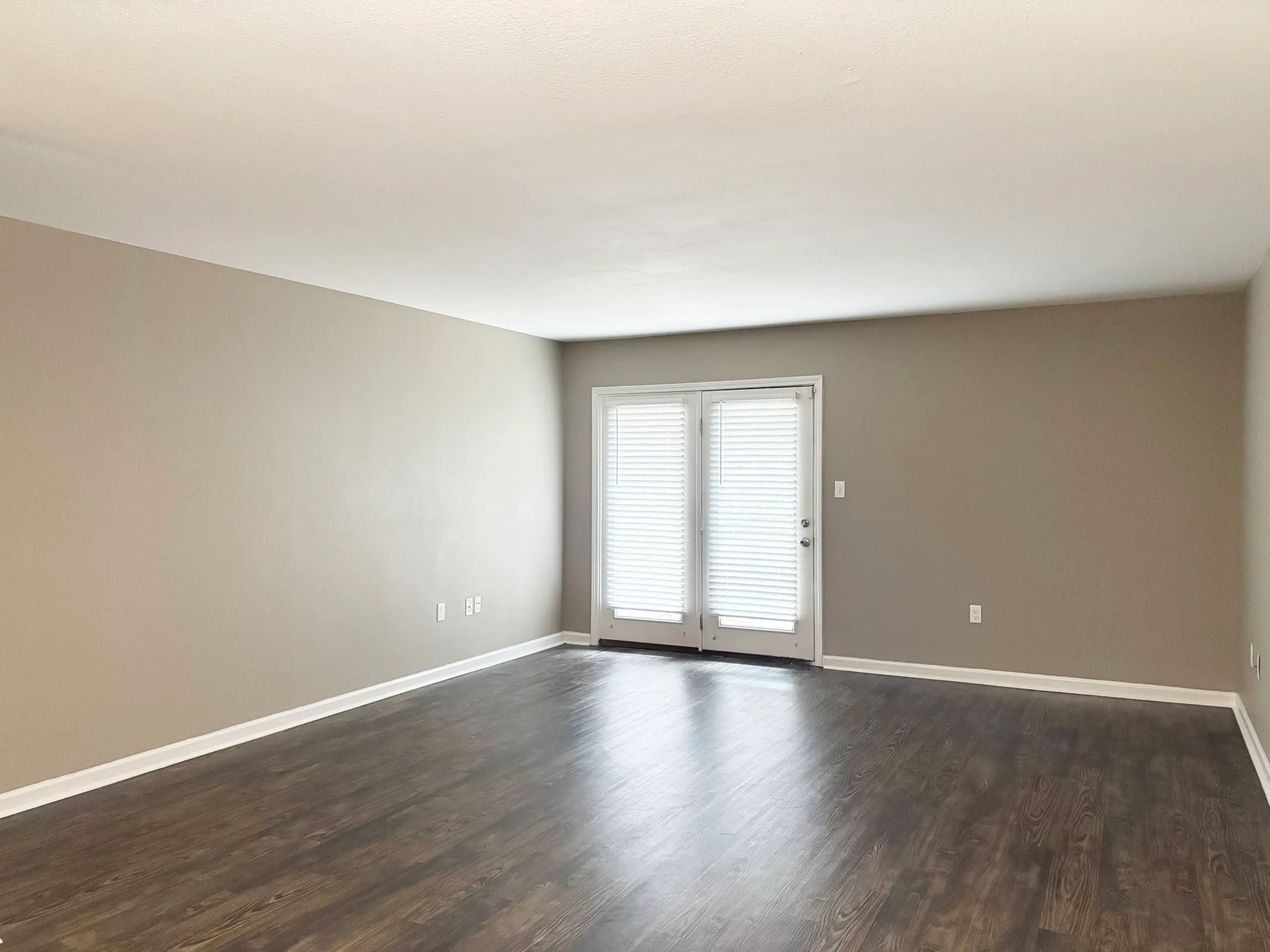Inviting living room with elegant wood flooring and abundant natural light from glass doors, perfect for a cozy apartment living.