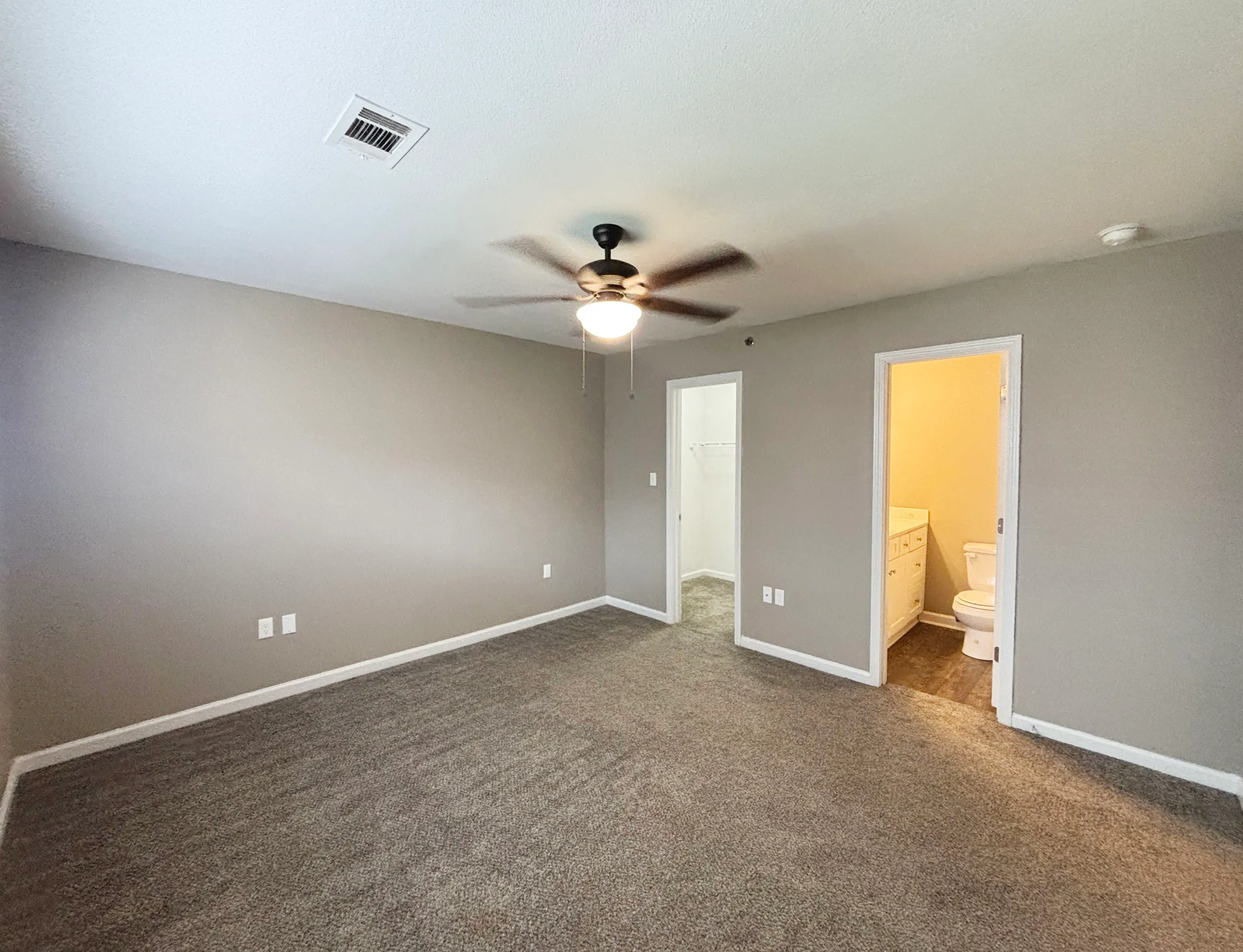 Spacious bedroom with plush carpet, elegant ceiling fan, and ensuite bathroom.