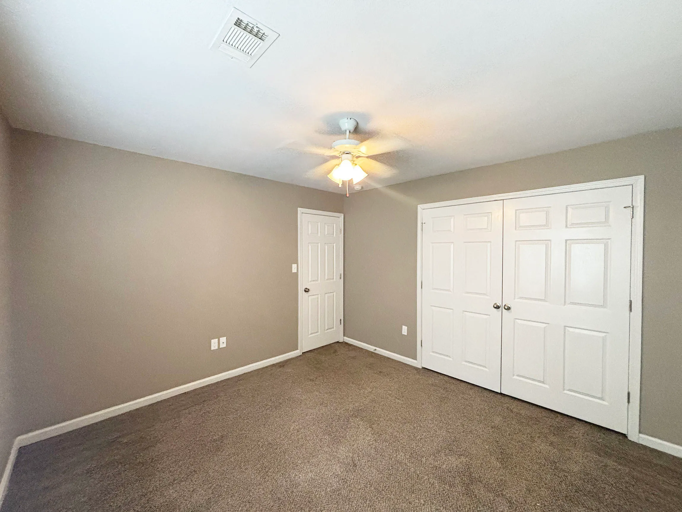 Bright and spacious bedroom with soft carpet flooring, neutral walls, and a ceiling fan, featuring double door closet for ample storage.