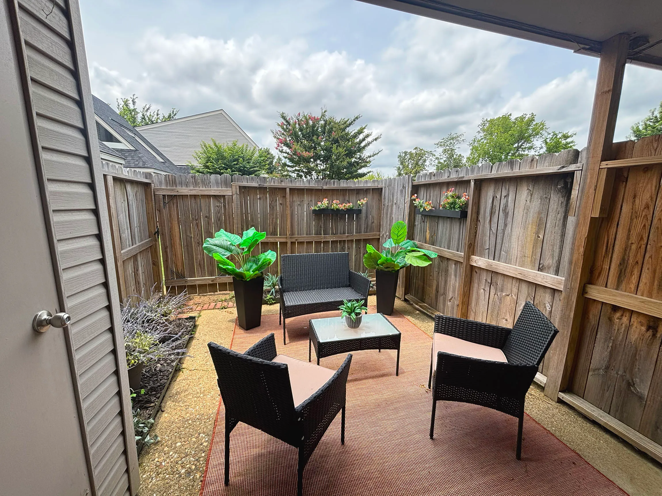 Charming private patio featuring cozy outdoor seating and vibrant potted plants, enclosed by a rustic wooden fence.