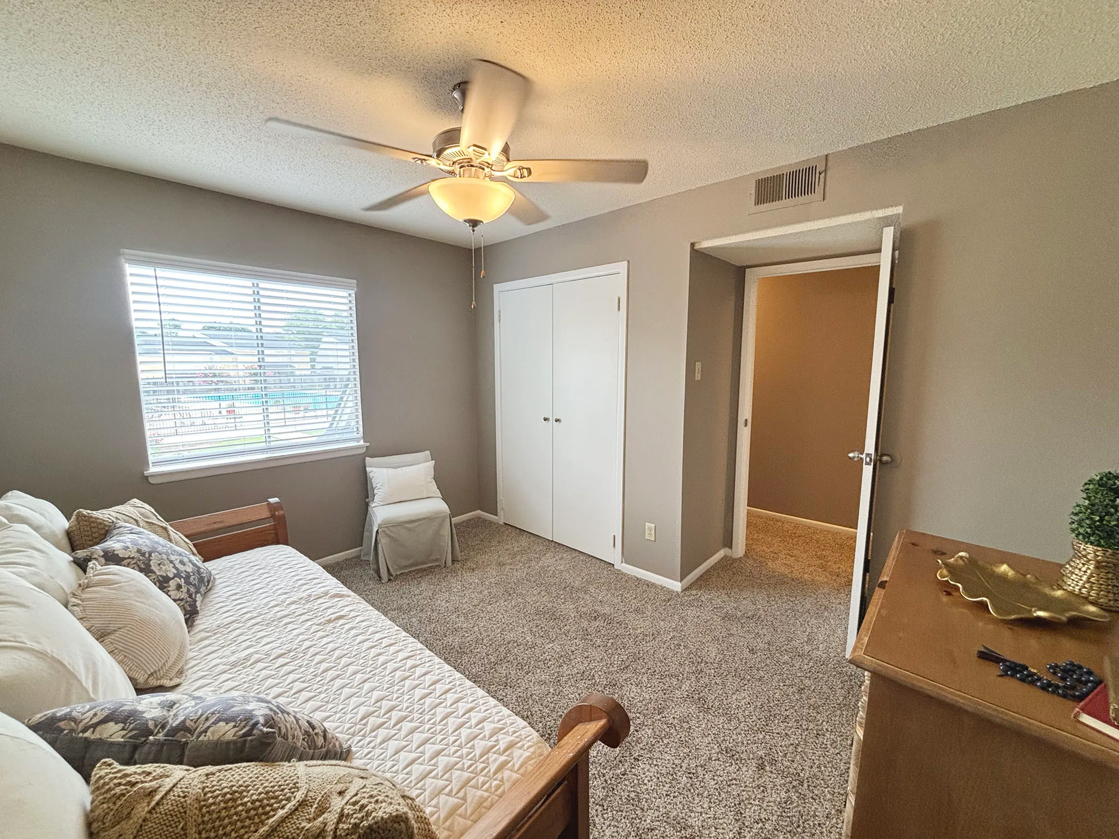 Inviting bedroom with a cozy bed, soft carpet, and natural light streaming in from a large window, creating a warm and welcoming atmosphere.