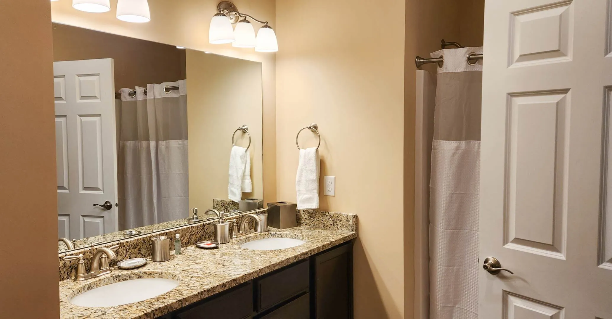 Elegant bathroom with granite countertop, dual sinks, and warm lighting, offering a spa-like retreat.