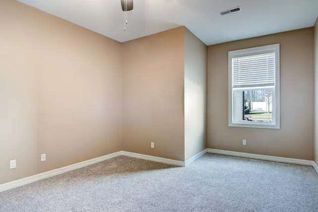 Bright and spacious room featuring plush carpet, neutral walls, and a large window with a serene outdoor view.