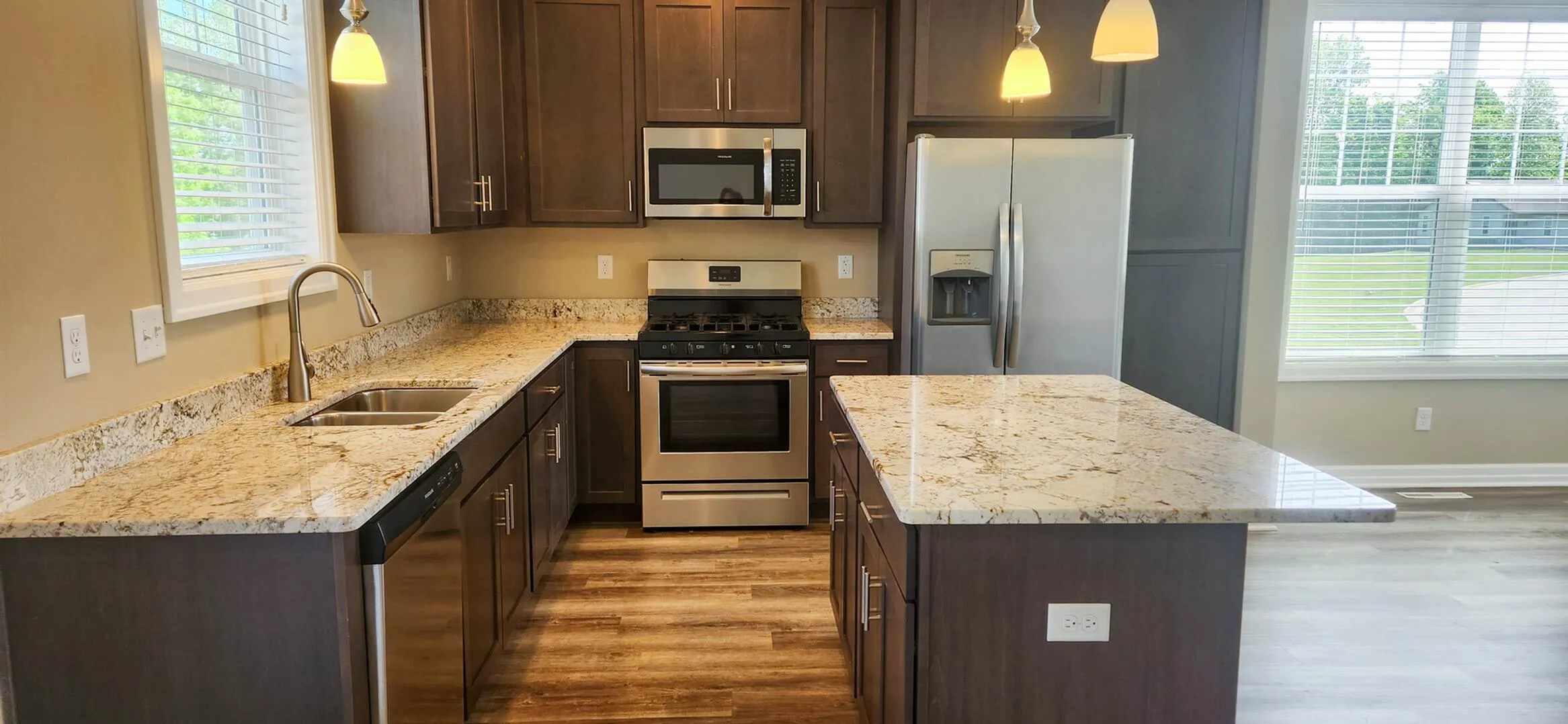 Modern kitchen with granite countertops, stainless steel appliances, and warm wooden cabinets, featuring ample natural light.