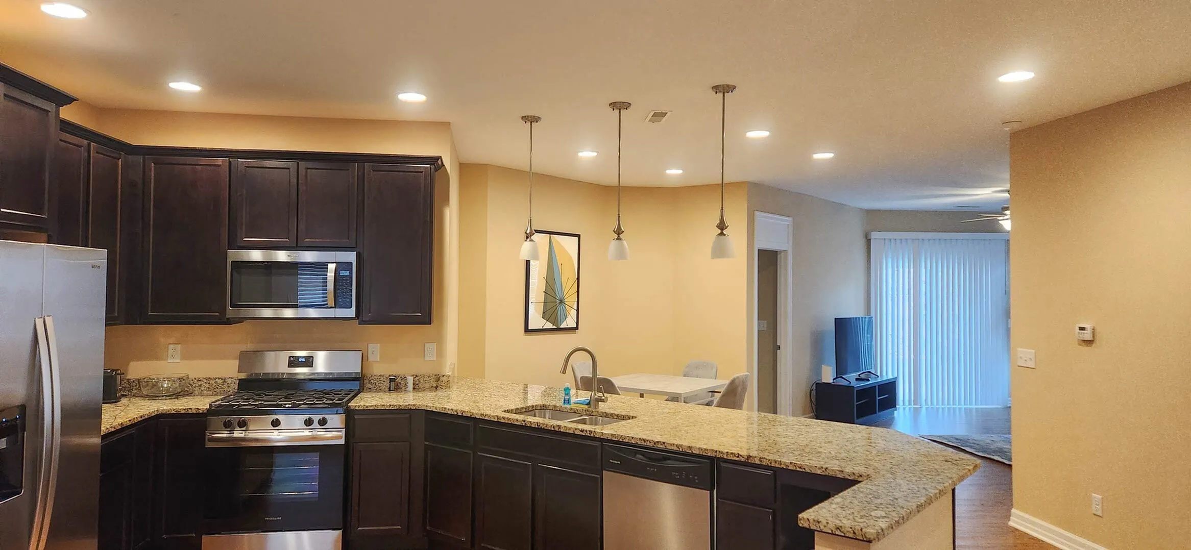 Modern kitchen with granite countertops, stainless steel appliances, and elegant pendant lighting opening to a cozy living area with natural light.