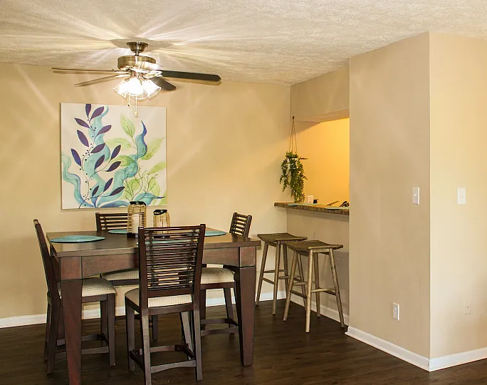 Inviting dining area with elegant wooden furniture and bright wall art, leading to a cozy kitchen with warm cabinetry.