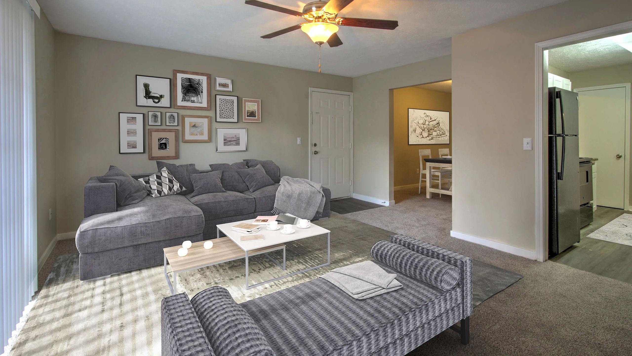 Inviting living space features a cozy gray sectional, modern wall art, ceiling fan, and a glimpse into the dining and kitchen areas.