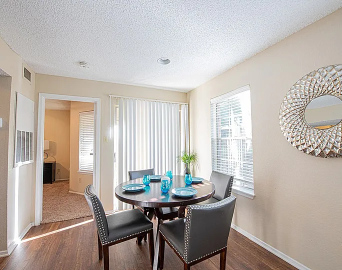 Bright dining area featuring a chic round table set with blue accents, surrounded by modern chairs, and a decorative wall mirror enhancing the spacious vibe.