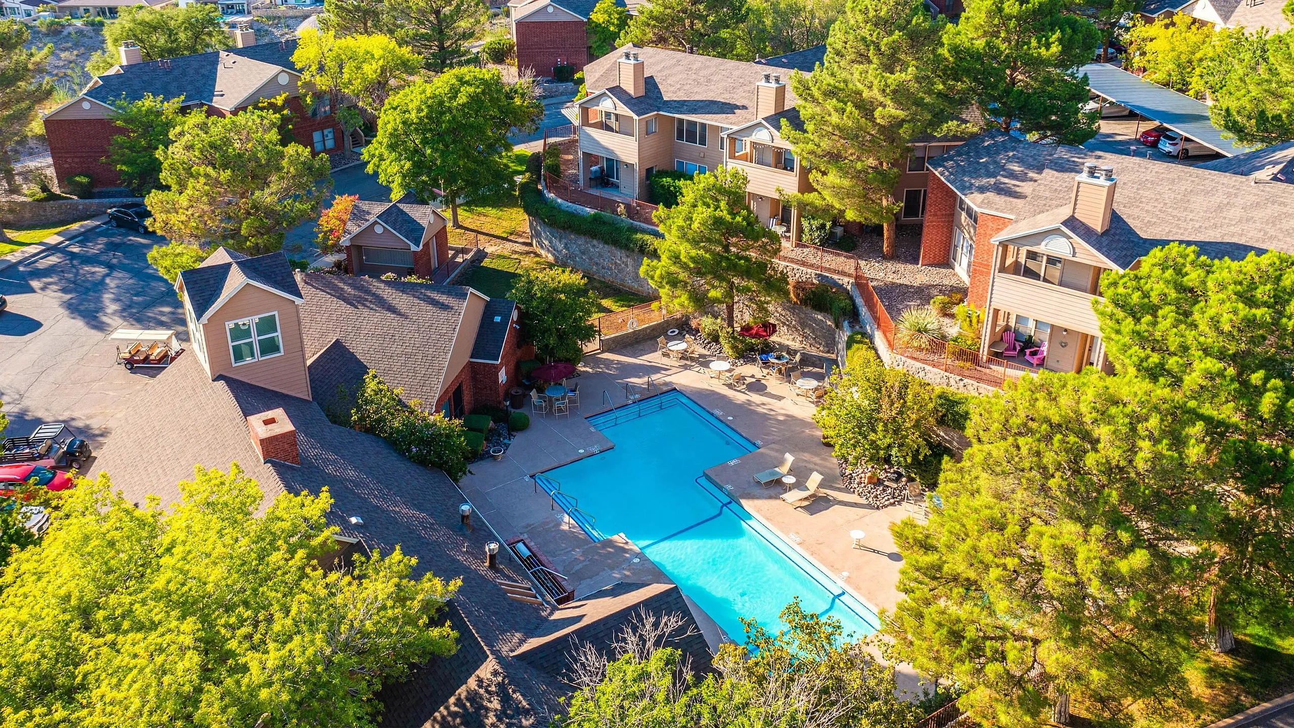 Vibrant aerial view of a picturesque apartment complex surrounded by lush greenery, featuring a sparkling outdoor pool and inviting communal spaces.