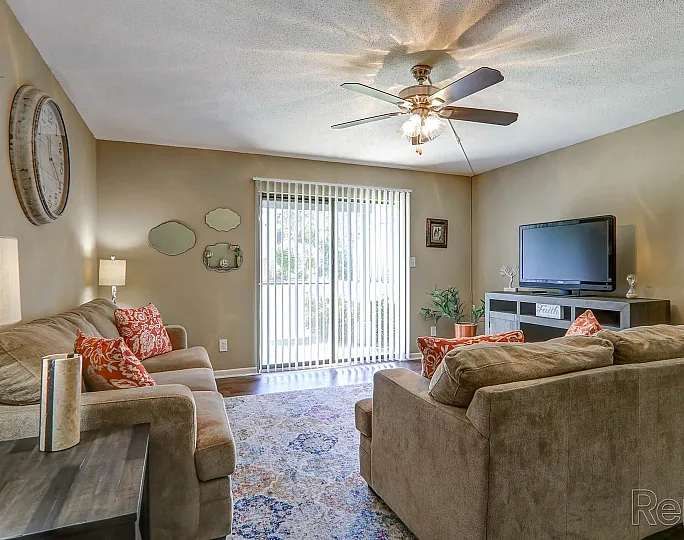 Cozy living room with plush sofas, vibrant pillows, and large TV, complemented by natural light through elegant sliding doors.