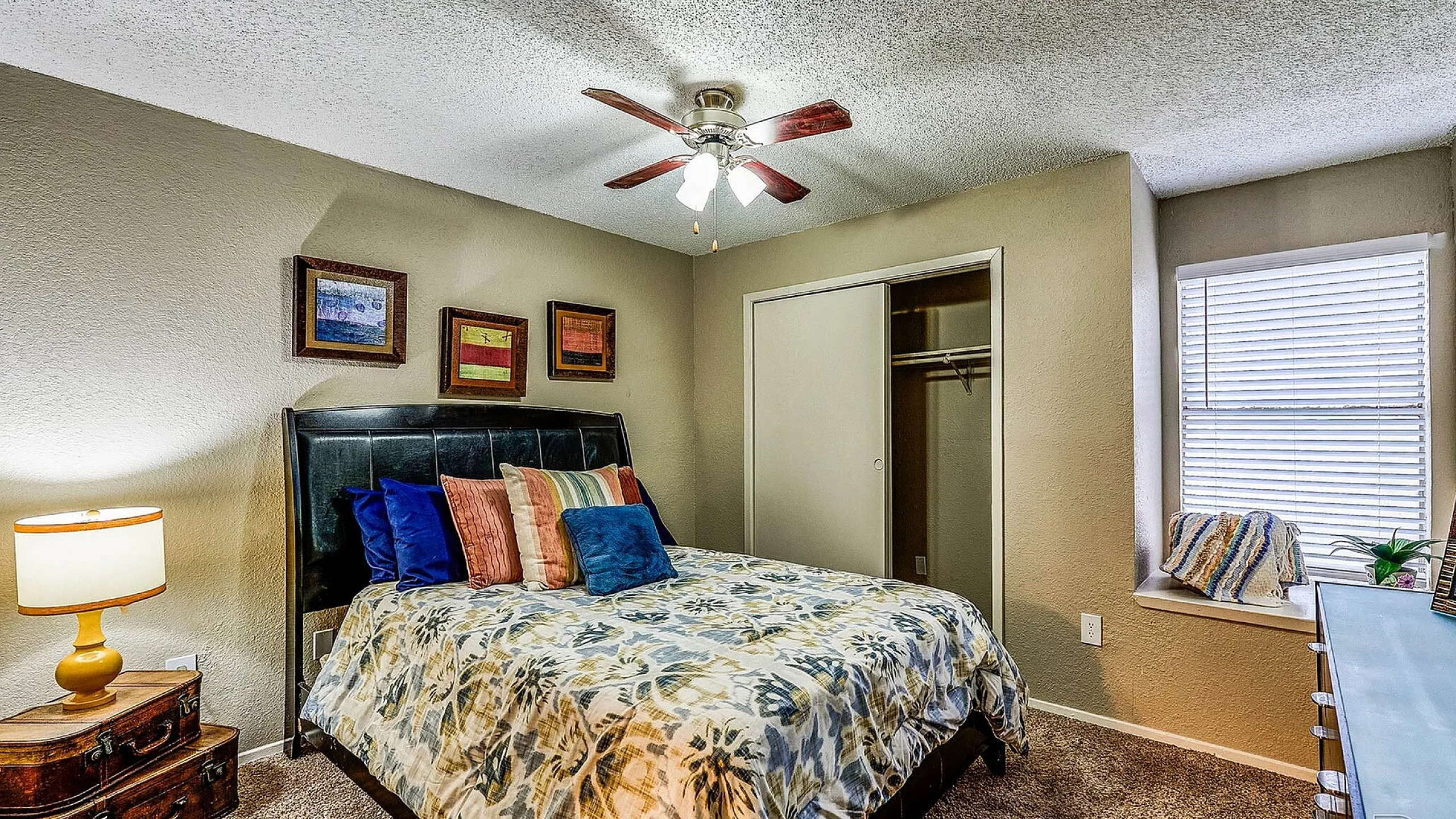 Charming bedroom with cozy decor, featuring a plush bed, vibrant throw pillows, ceiling fan, and warm lighting, creating a welcoming atmosphere.