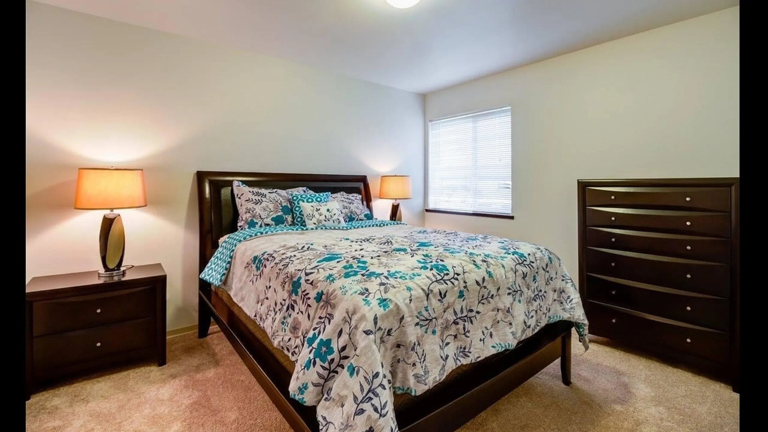 Inviting bedroom with elegant dark wood furniture, a plush bed adorned with vibrant floral bedding, and soft ambient lighting.