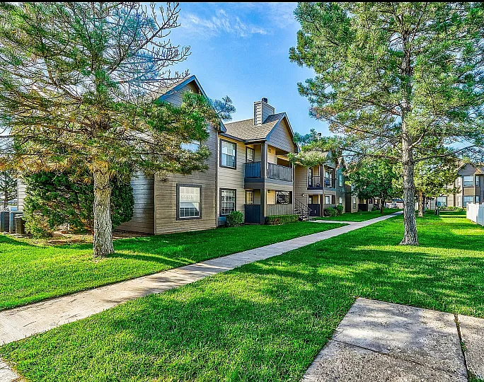 Charming apartment exterior nestled in lush green landscape with mature trees, showcasing a serene community ambiance.