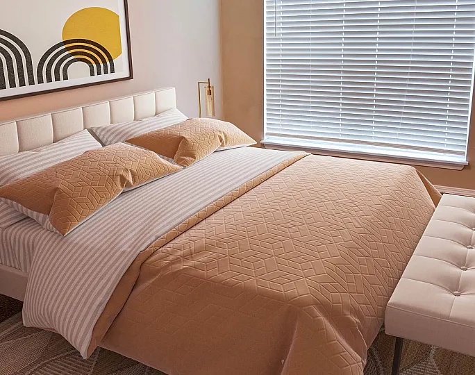 Cozy bedroom featuring a modern bed with stylish geometric bedding, complemented by a chic bench and contemporary art under natural light.