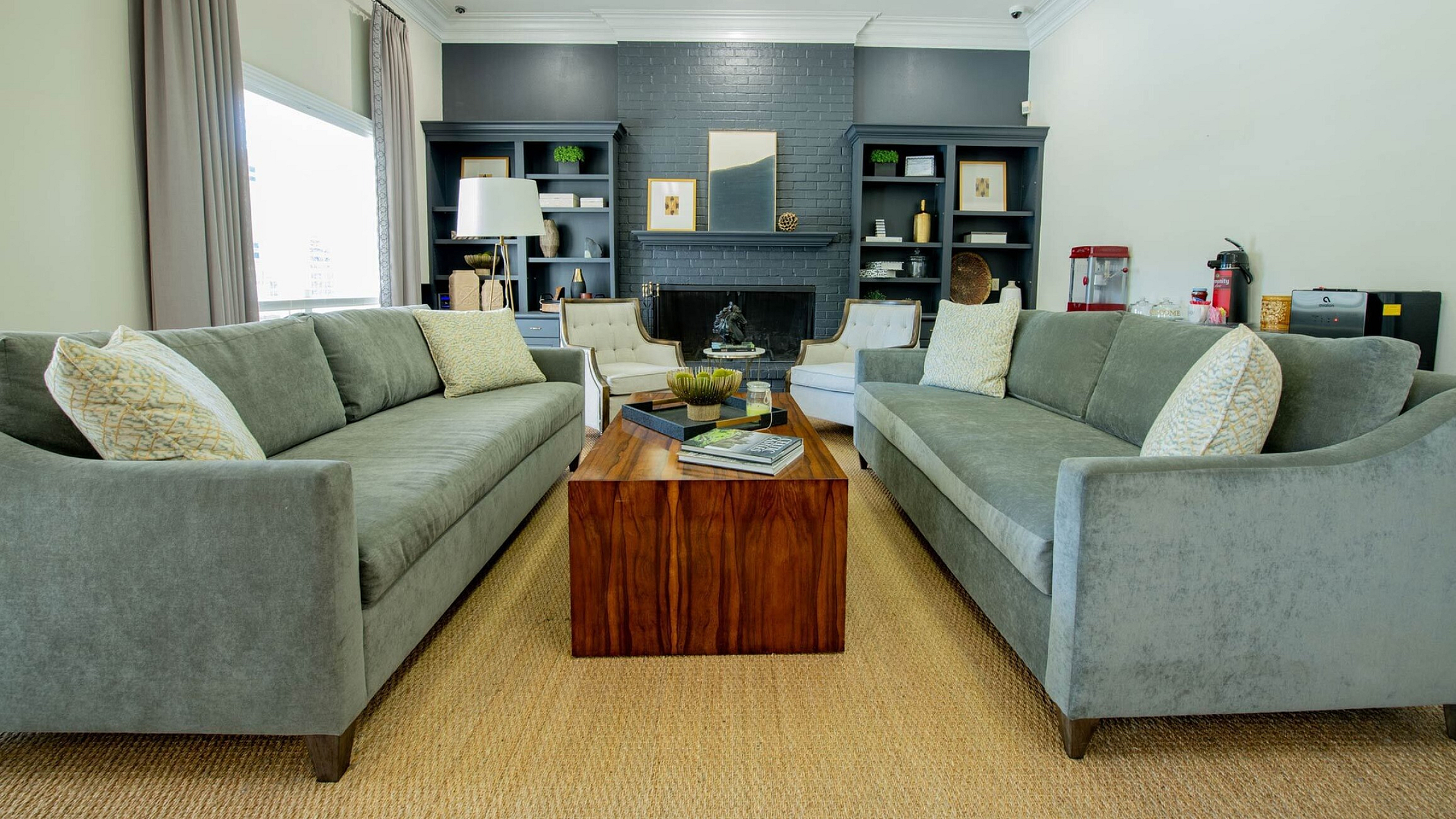 Elegant living room showcasing two plush grey sofas, a sleek wooden coffee table, and a cozy fireplace accented with artistic decor and built-in shelving.