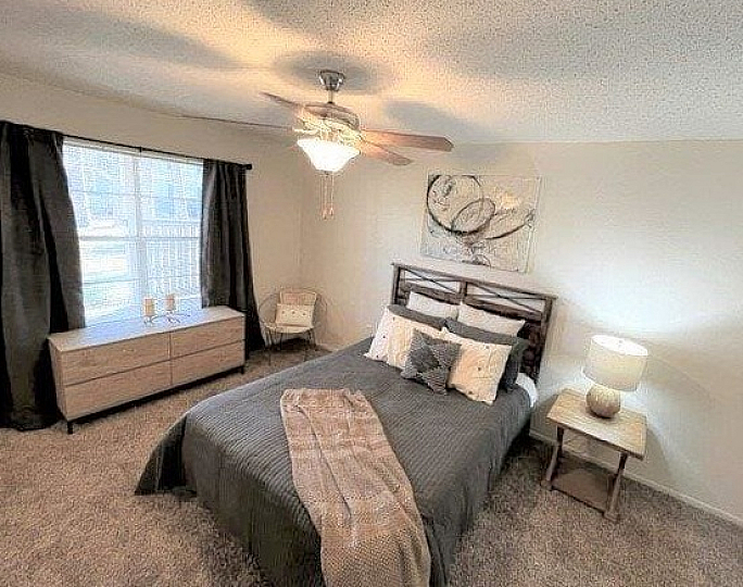 Cozy bedroom with chic decor, featuring a comfortable bed, modern lighting, and inviting natural light through a large window.