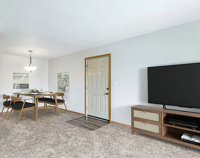 Inviting living and dining area featuring plush carpeting, chic wooden furniture, and a large modern TV for comfortable relaxation.