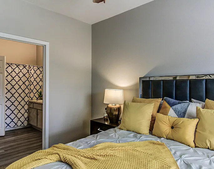 Inviting bedroom with plush pillows and cozy lighting, leading to a stylish bathroom with contemporary decor.