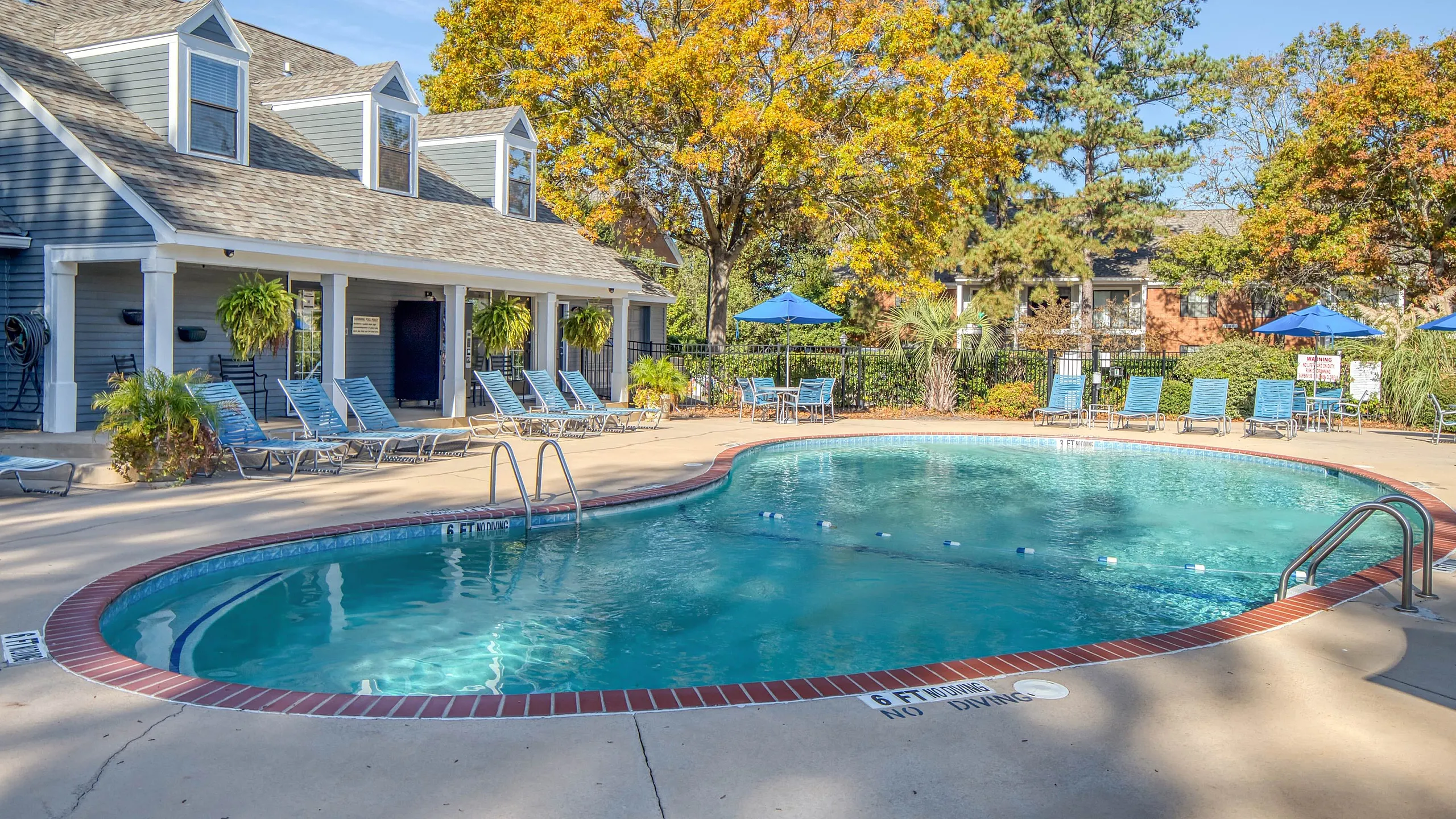 Charming outdoor pool area surrounded by lush trees, offering plenty of poolside seating and a serene ambiance.