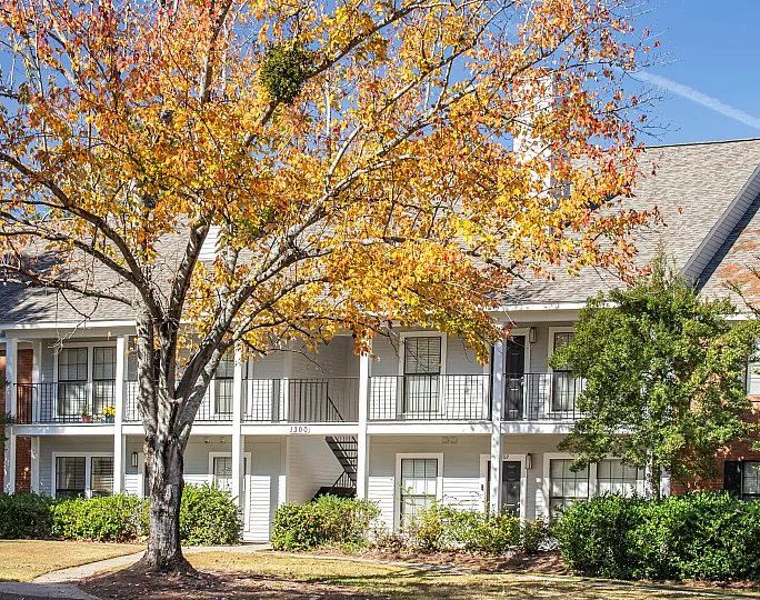 Charming two-story apartment building with a welcoming facade, surrounded by lush greenery and vibrant autumn foliage.