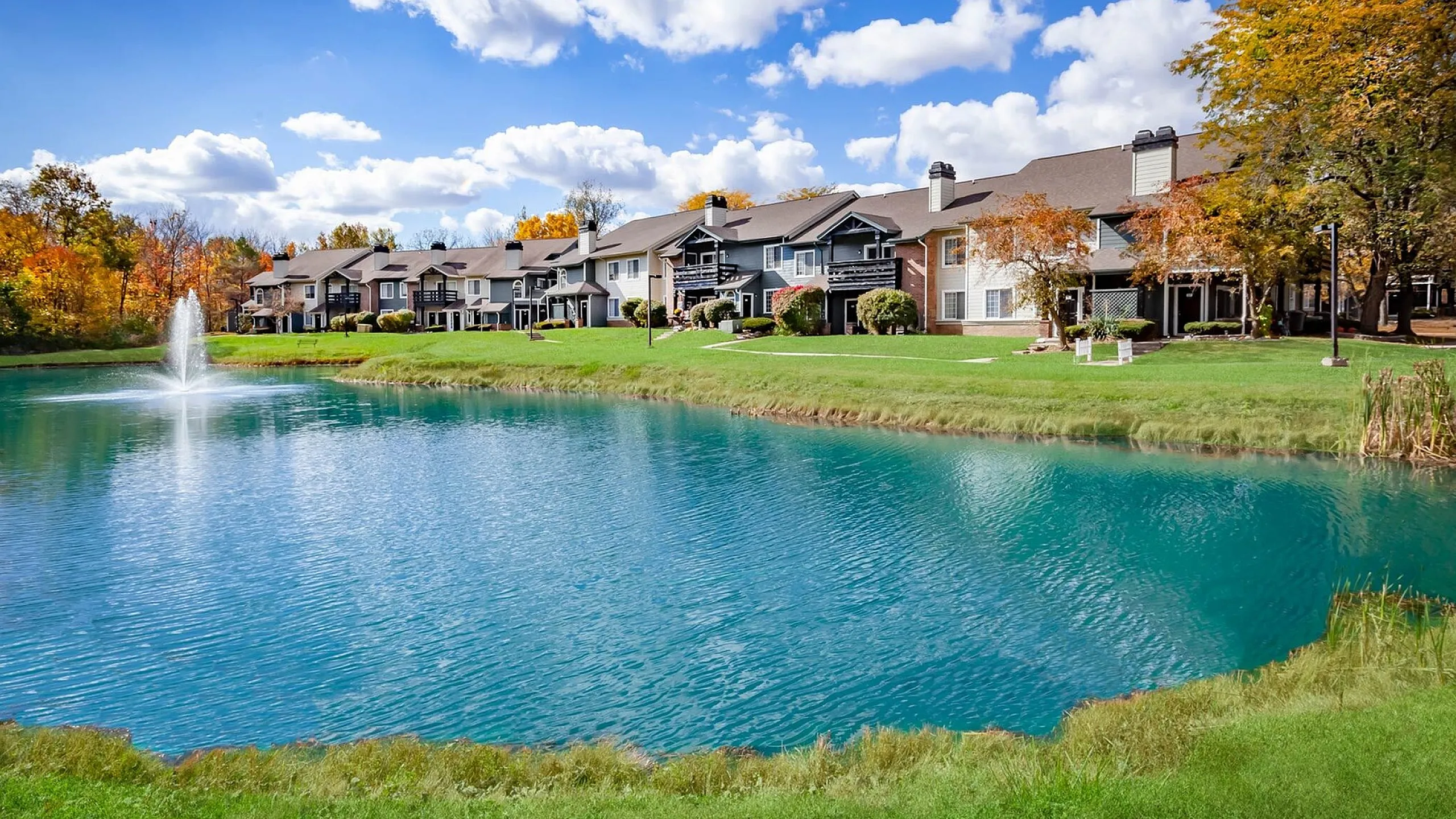 Charming lakeside apartments featuring picturesque views, lush greenery, and vibrant fall colors under a clear blue sky.