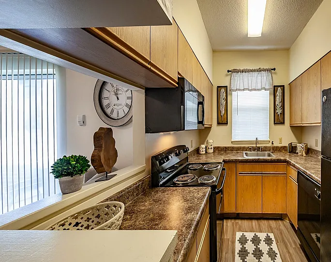 Charming modern kitchen with warm wood cabinetry, sleek black appliances, and a cozy window view.