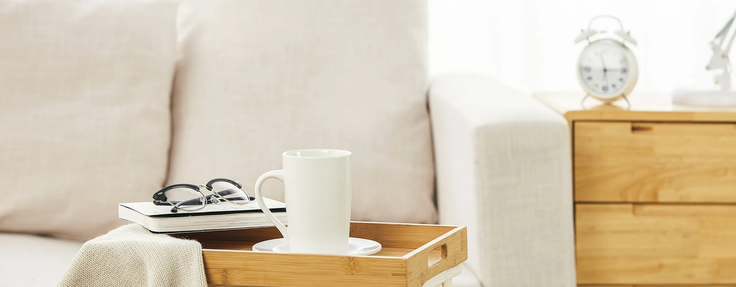 Chic and cozy living space with a soft, beige sofa, stylish wooden tray with a white mug, and modern lamp creating a serene ambiance.