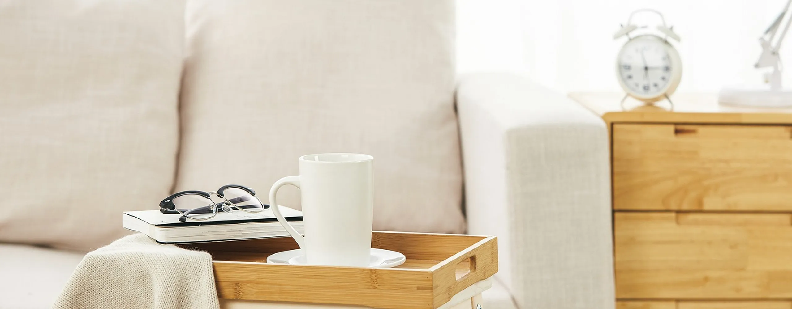 Inviting living space showcasing a cozy beige sofa, chic wooden tray with a coffee mug, and elegant decor on a light wood side table.