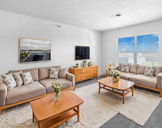 Bright and inviting living room with contemporary sofas, elegant wood coffee tables, and large window offering serene views.