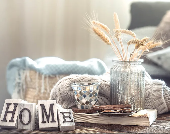 Charming home decor featuring a cozy arrangement with a glass jar of wheat stems, a silver candle holder, and 'HOME' letter blocks on a rustic wooden table.