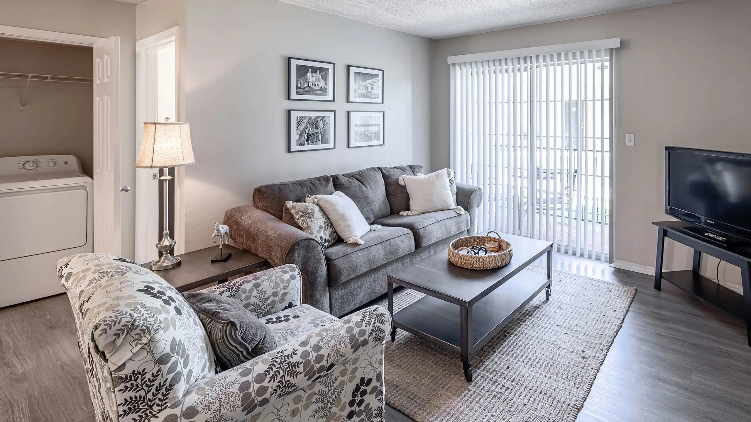 Modern living room with cozy gray sofa, stylish armchair, and sleek entertainment setup, complemented by elegant decor and natural light streaming through vertical blinds.