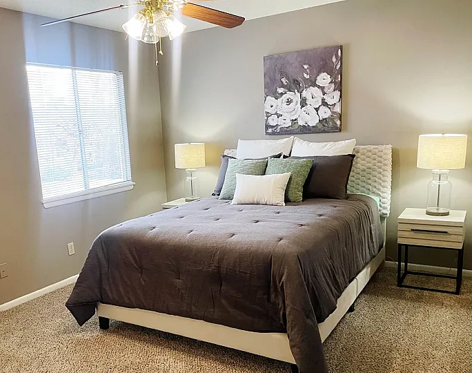 Cozy bedroom with elegant gray bedding, modern side tables, and chic floral art, illuminated by warm natural light and stylish lamps.