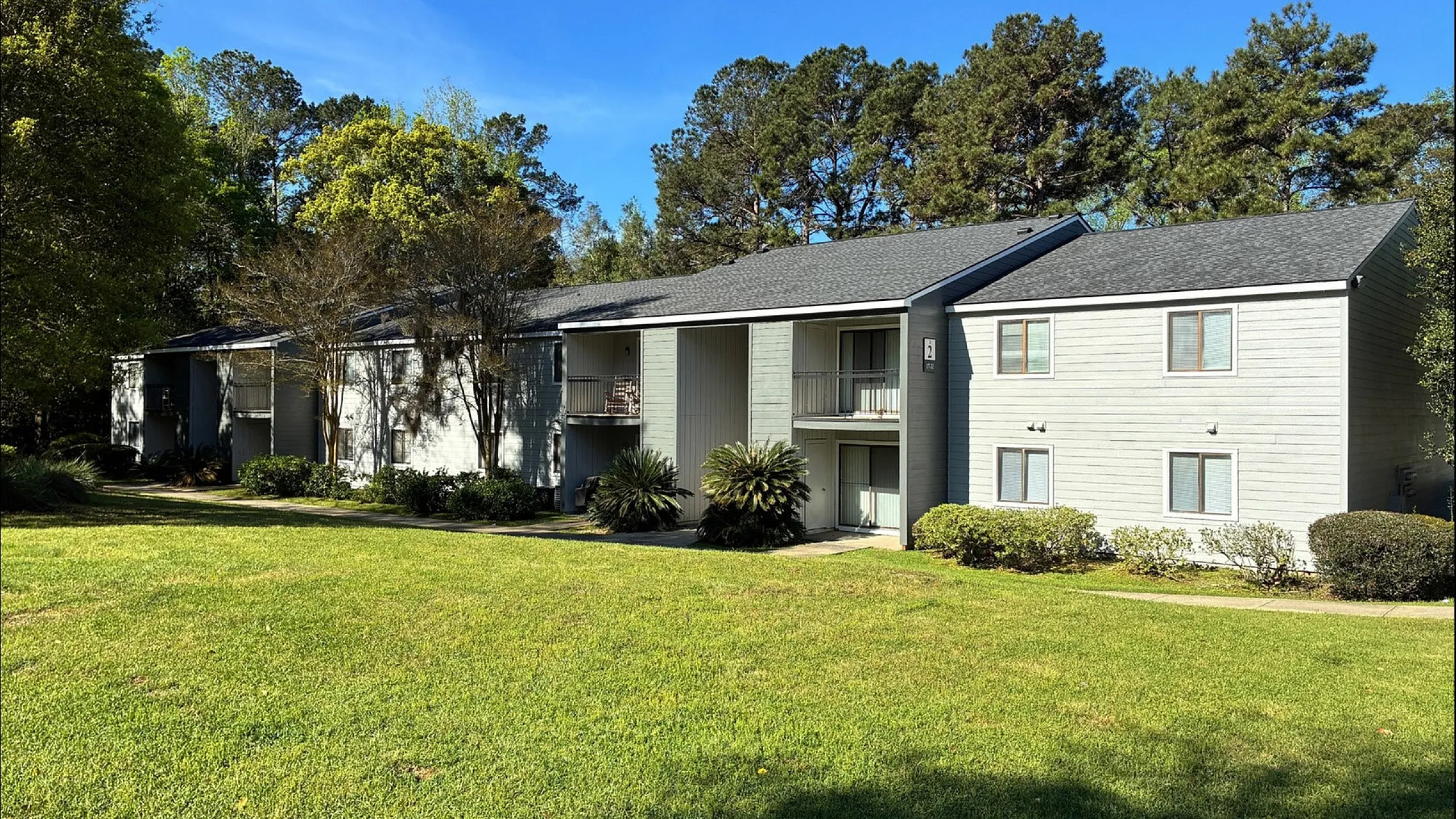 Charming apartment complex surrounded by lush greenery, featuring spacious balconies and large windows, perfect for tranquil living.