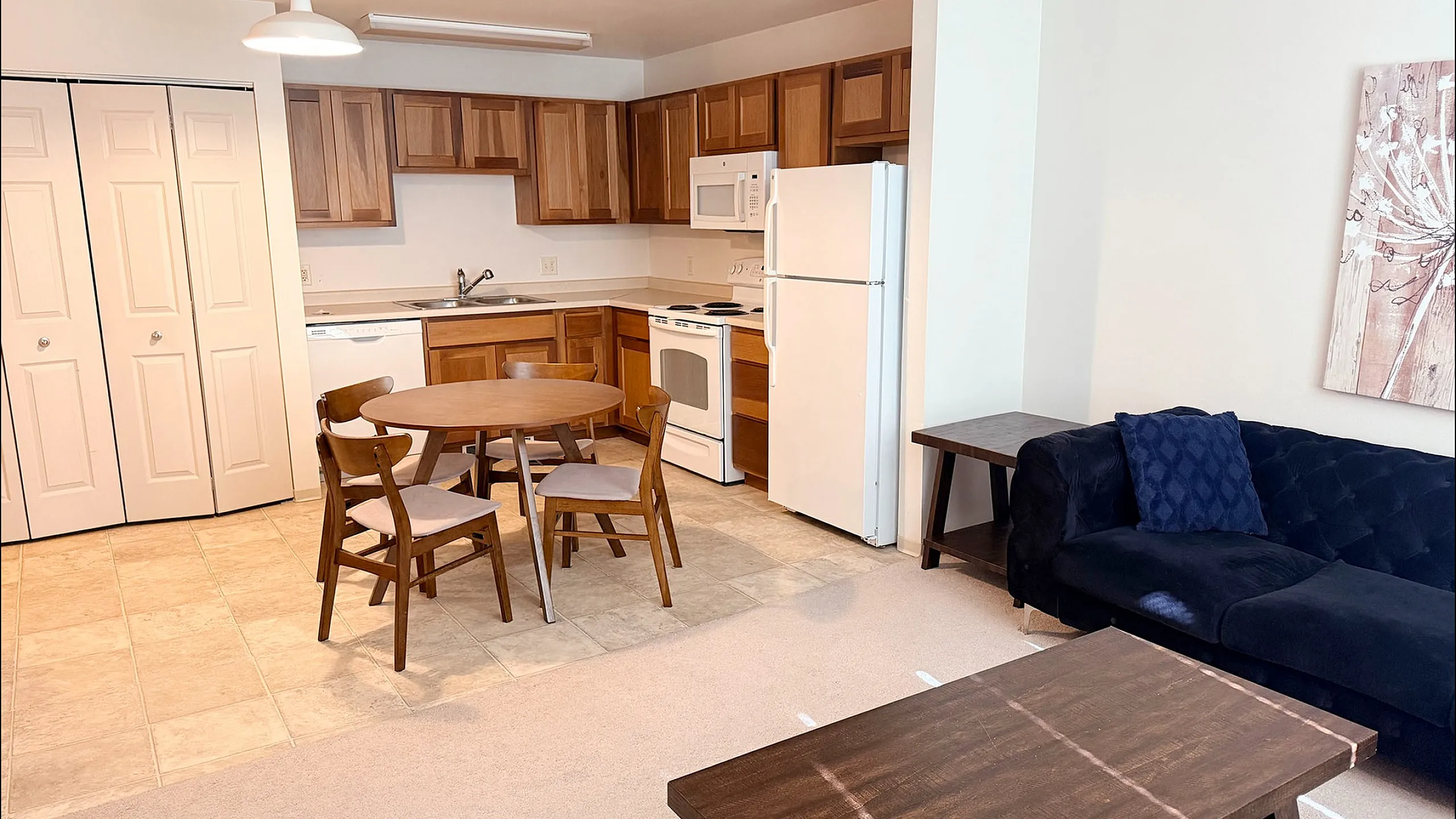 Inviting open-plan living space featuring a cozy kitchen with wooden cabinetry, charming dining area, and sleek navy sofa.