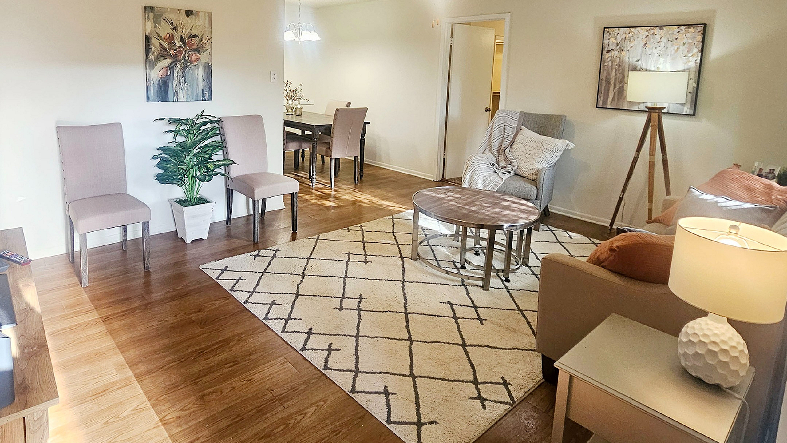 Bright and inviting living area with modern decor, warm lighting, and open dining space featuring elegant chairs and wooden flooring.