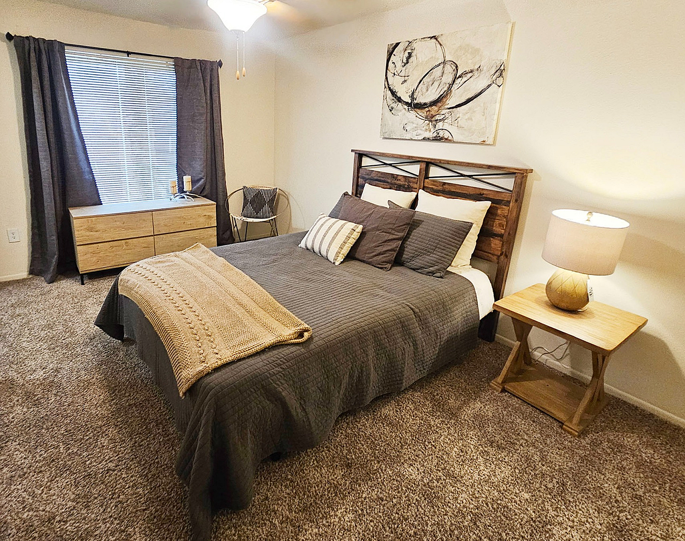 Cozy and stylish bedroom with plush carpet, featuring a large bed with elegant wooden headboard, a modern nightstand with a lamp, and tasteful artwork on the wall.