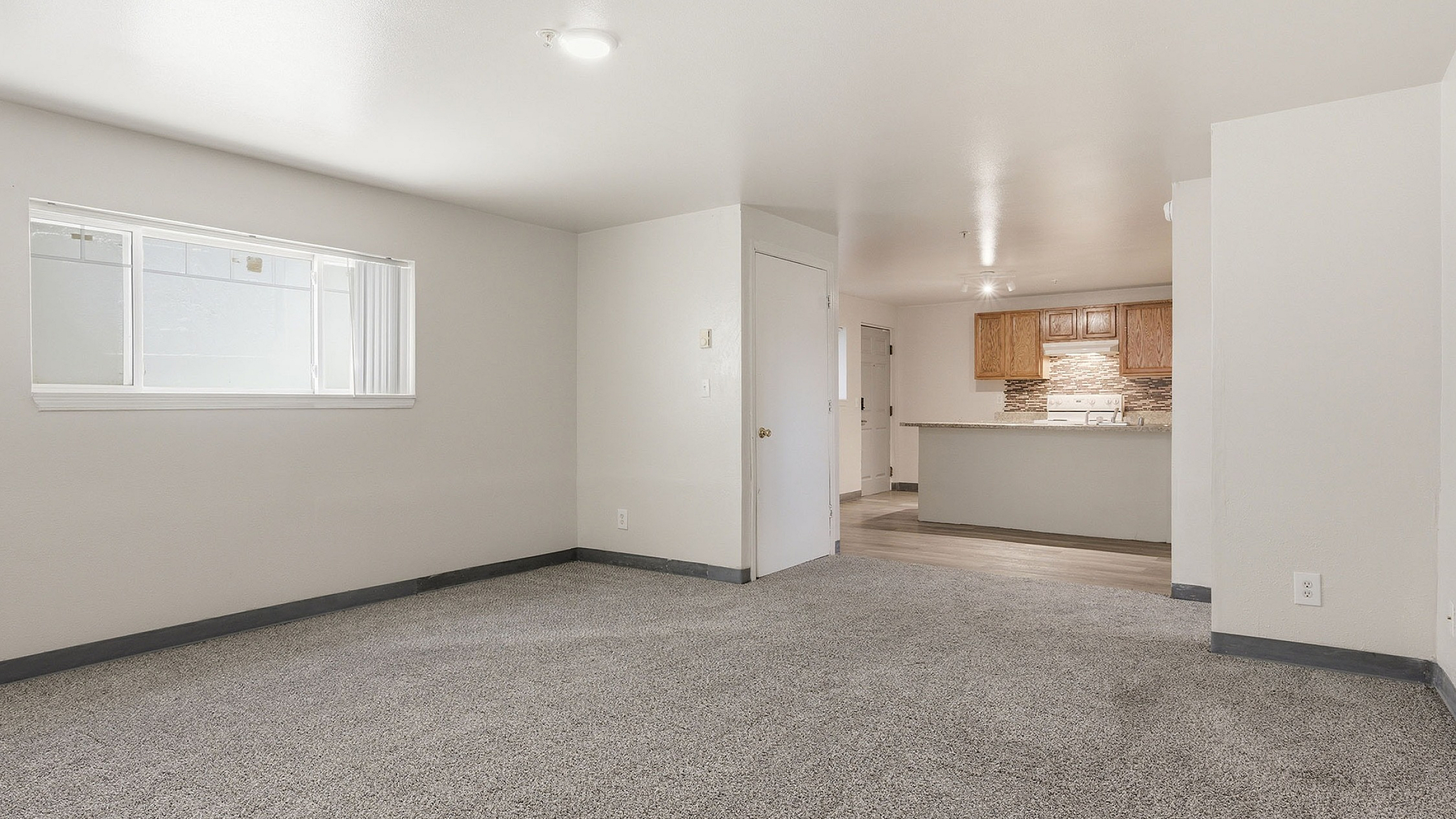 Bright living space with plush carpeting and a modern open-concept kitchen featuring wooden cabinetry and stylish backsplash.