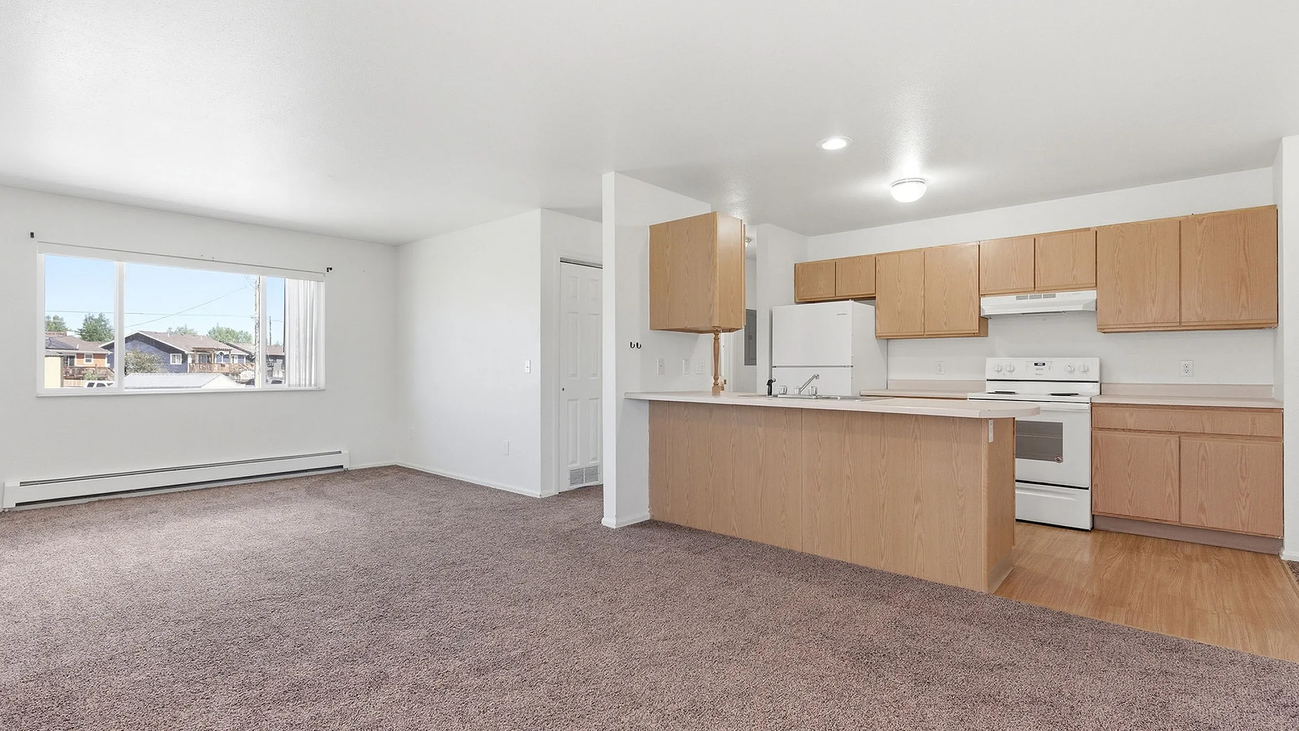 Bright open-concept living area featuring a modern kitchen with wooden cabinetry and large window views.