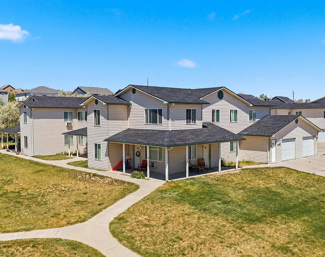 Charming suburban homes with spacious driveways and inviting front porches, nestled in a peaceful neighborhood under a bright blue sky.