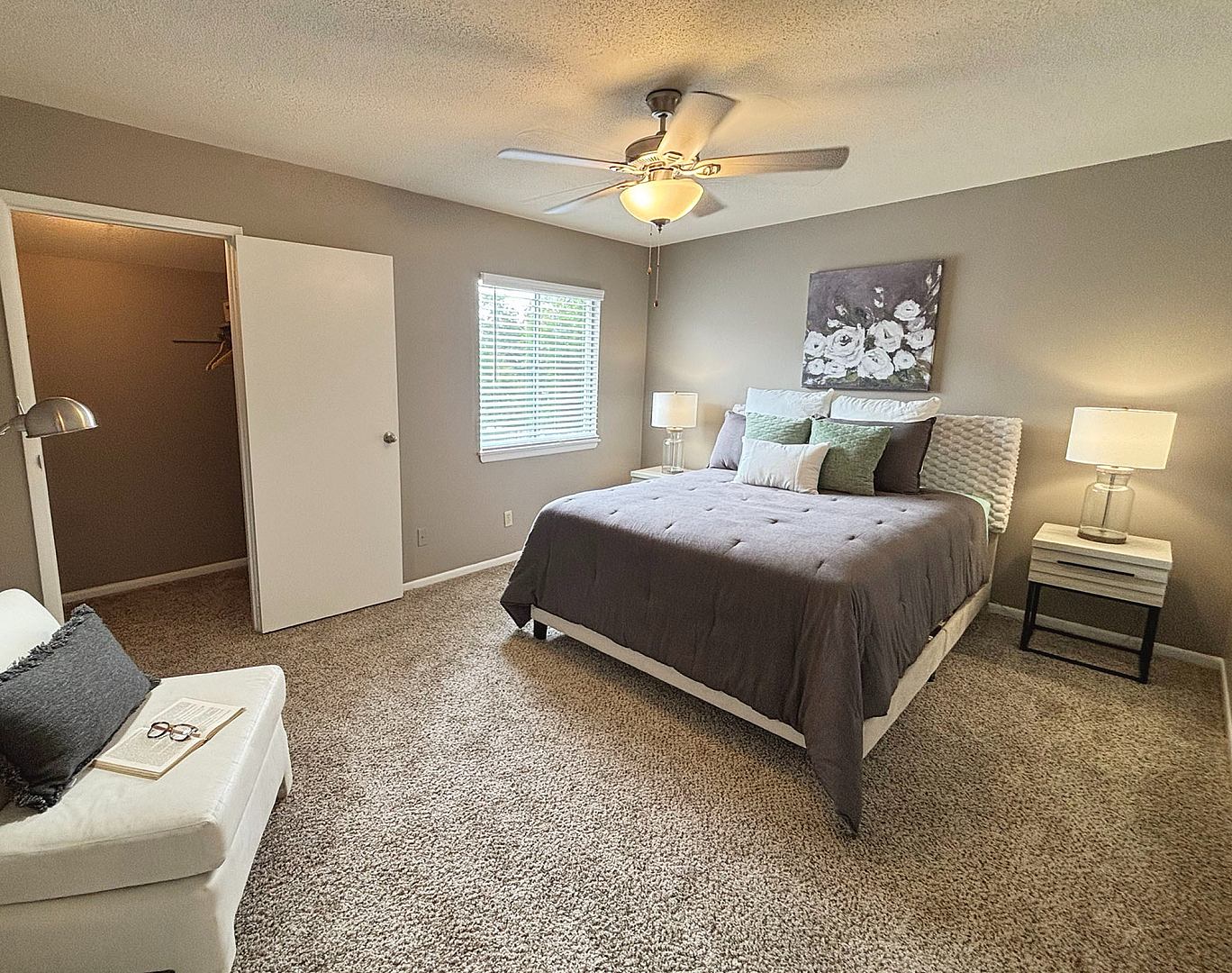 Inviting bedroom with plush carpet, elegant lighting, cozy sitting area, and a spacious walk-in closet.