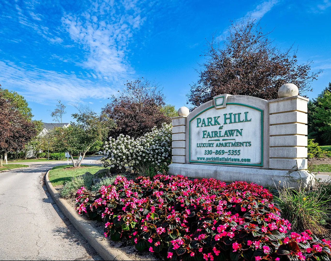 Entrance to Park Hill at Fairlawn Luxury Apartments, featuring vibrant flowerbeds under a bright blue sky.